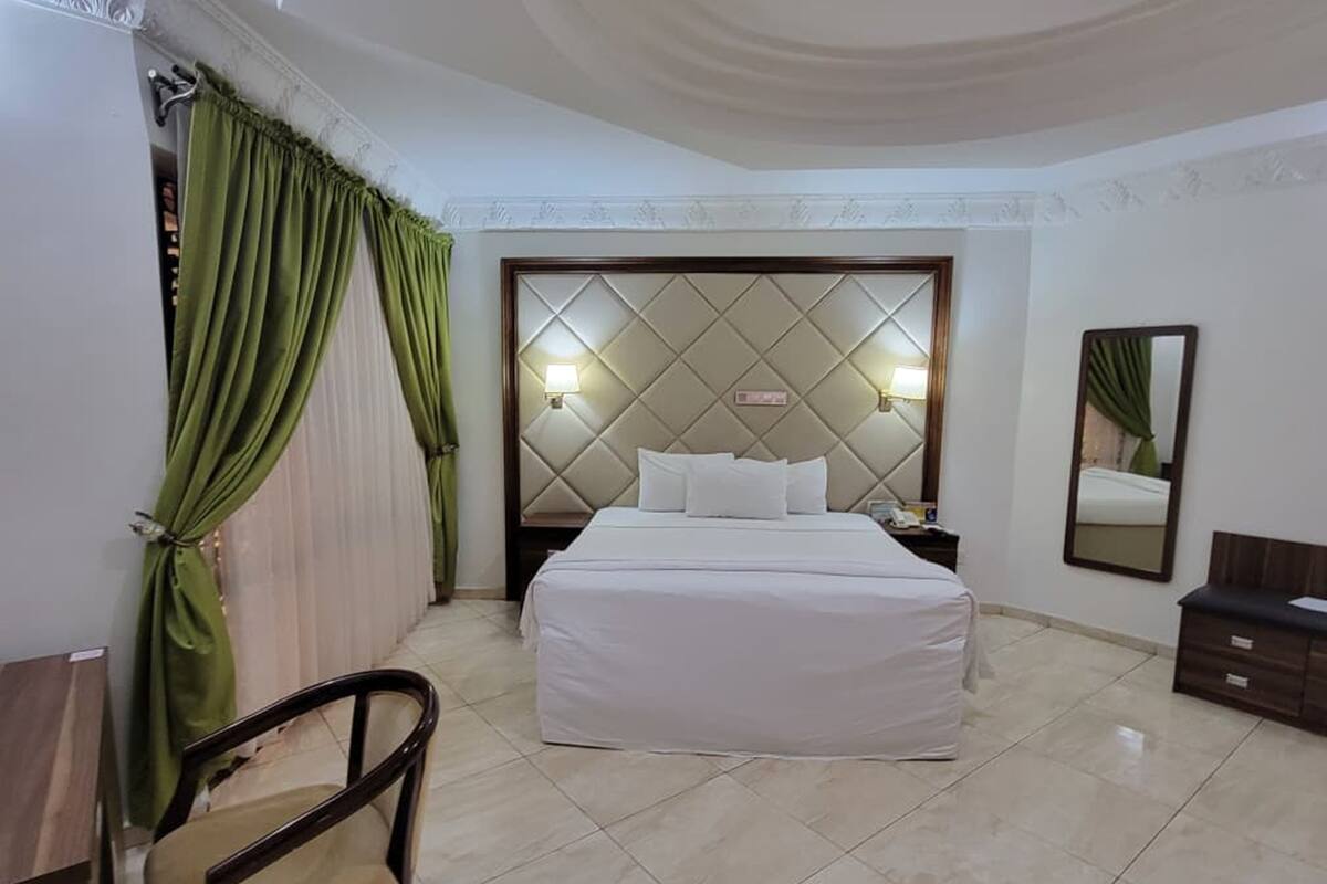 Ein Hotelzimmer mit einem Bett, einem Nachttisch, einem Stuhl, einem Spiegel und grünen Vorhängen.