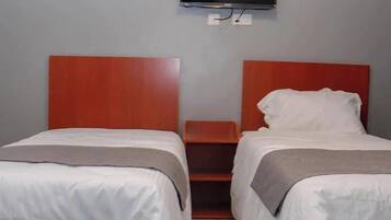Una habitación de hotel con dos camas individuales, un televisor montado en la pared y una mesita de noche de madera entre las camas.