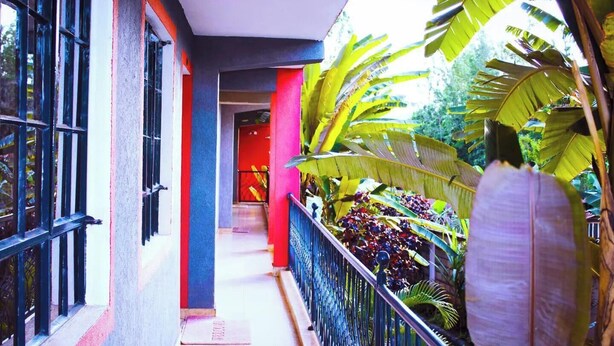 A narrow corridor with a red door, surrounded by lush tropical plants and a metal railing. - Camsupreme Studios Meru  (Meru)