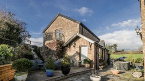 Ein Haus aus Stein mit einem geneigten Dach, einem kleinen Balkon und einem Garten mit Blumentöpfen.