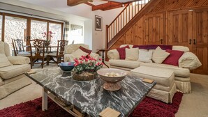 Ein geräumiges Wohnzimmer mit hoher Decke, Holzbalken, einer Treppe und einem großen Fenster.
