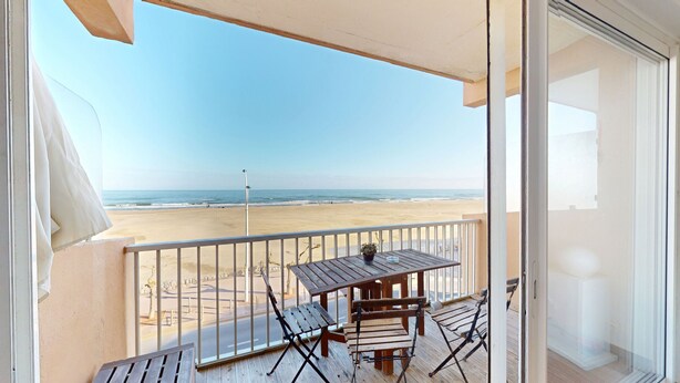 A balcony with a wooden table and chairs, overlooking a beach. - Seafront apartment for 4 people (Canet-en-Roussillon)