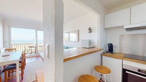 A modern kitchen with a wooden countertop, a built-in oven, and a coffee maker. There is a dining area with a table and chairs, and a view of the ocean through a large window. - Seafront apartment for 4 people (Canet-en-Roussillon)