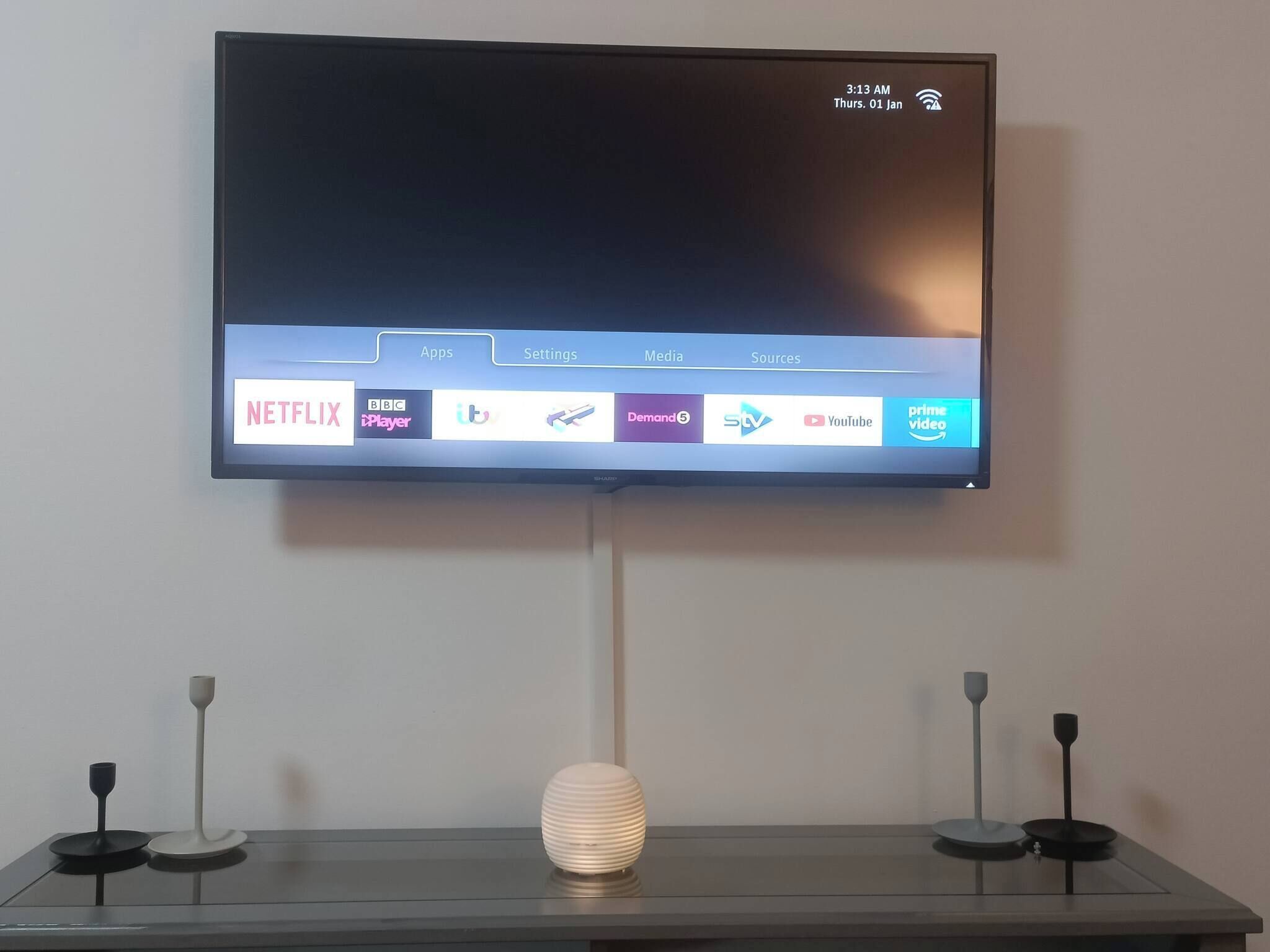 A flat-screen TV mounted on a wall displaying a media interface with various streaming services.