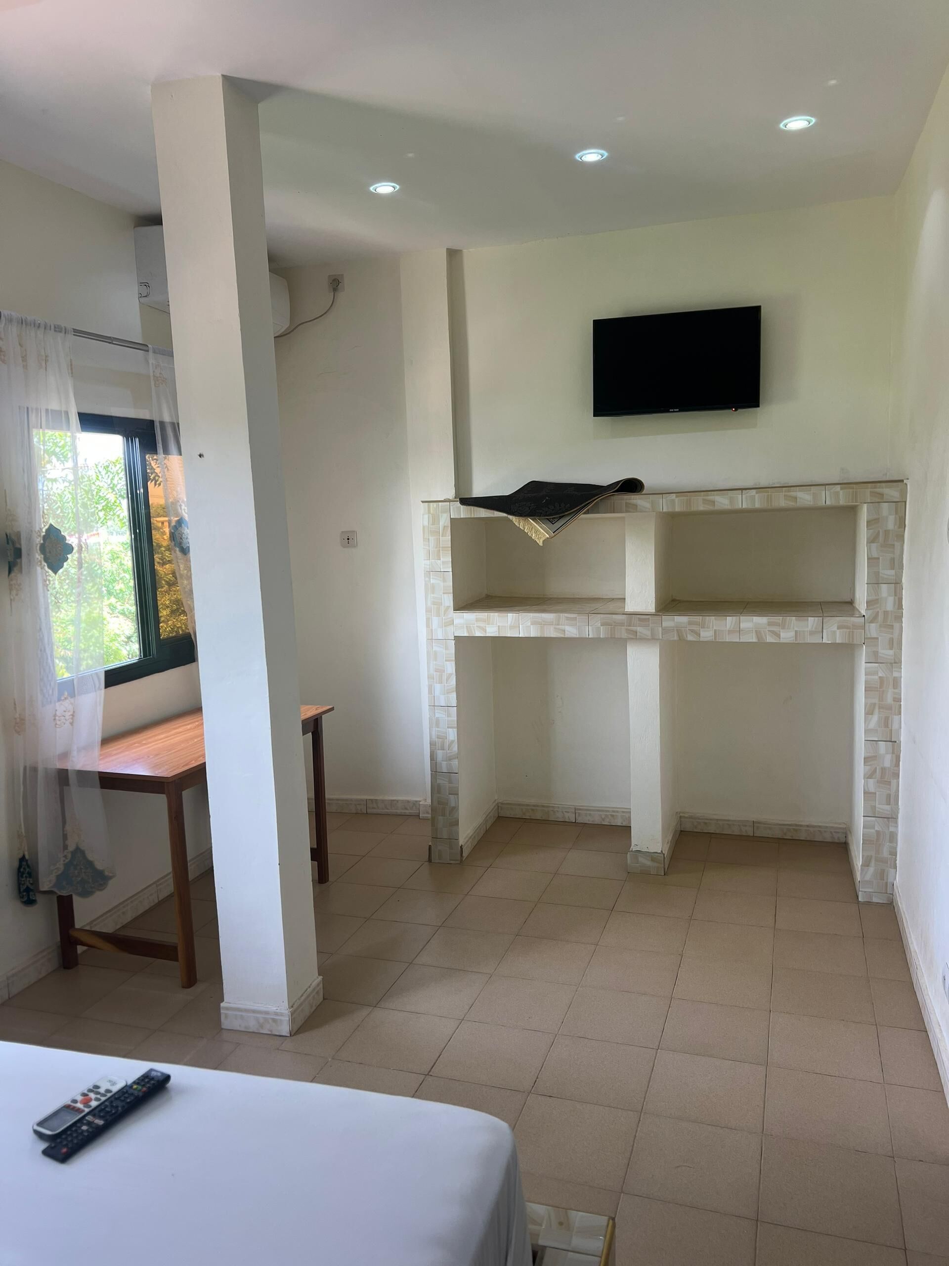 A hotel room with a bed, a TV mounted on the wall, a small table, and a window with curtains.