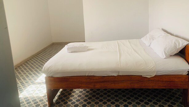 A small, single-bed room with a wooden frame, white bedding, and patterned floor tiles. - Hôtel ESCALE (Sindia)