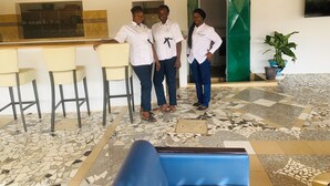 A reception area with a bar, three people in uniform, and a patterned floor. - Hôtel ESCALE (Sindia)