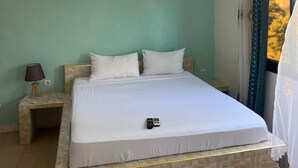 Una habitación de hotel con cama, mesita de noche, lámpara y ventana con cortinas.