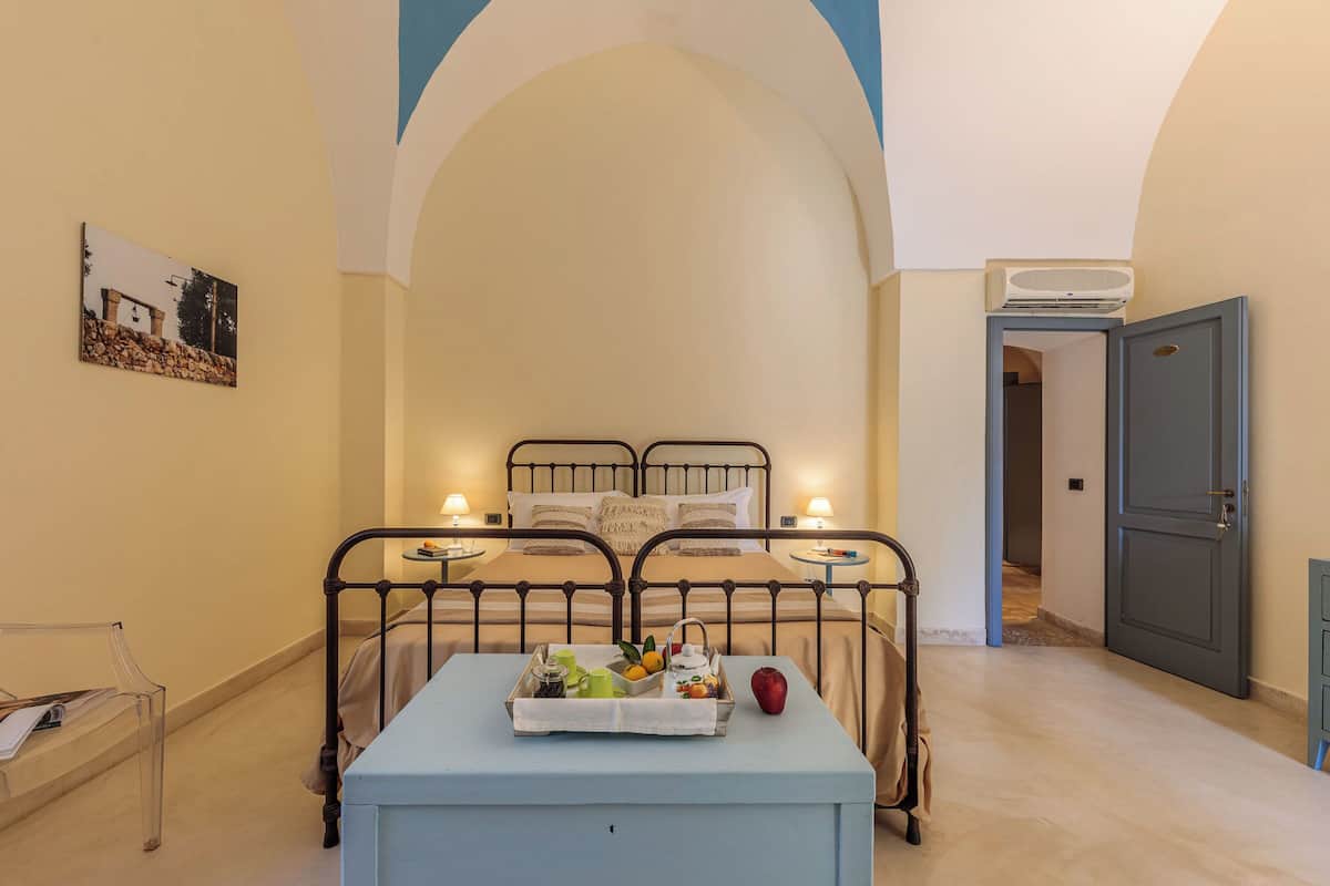 A bedroom with two beds, a bedside table with a tray of fruits and a teapot, and a picture on the wall.