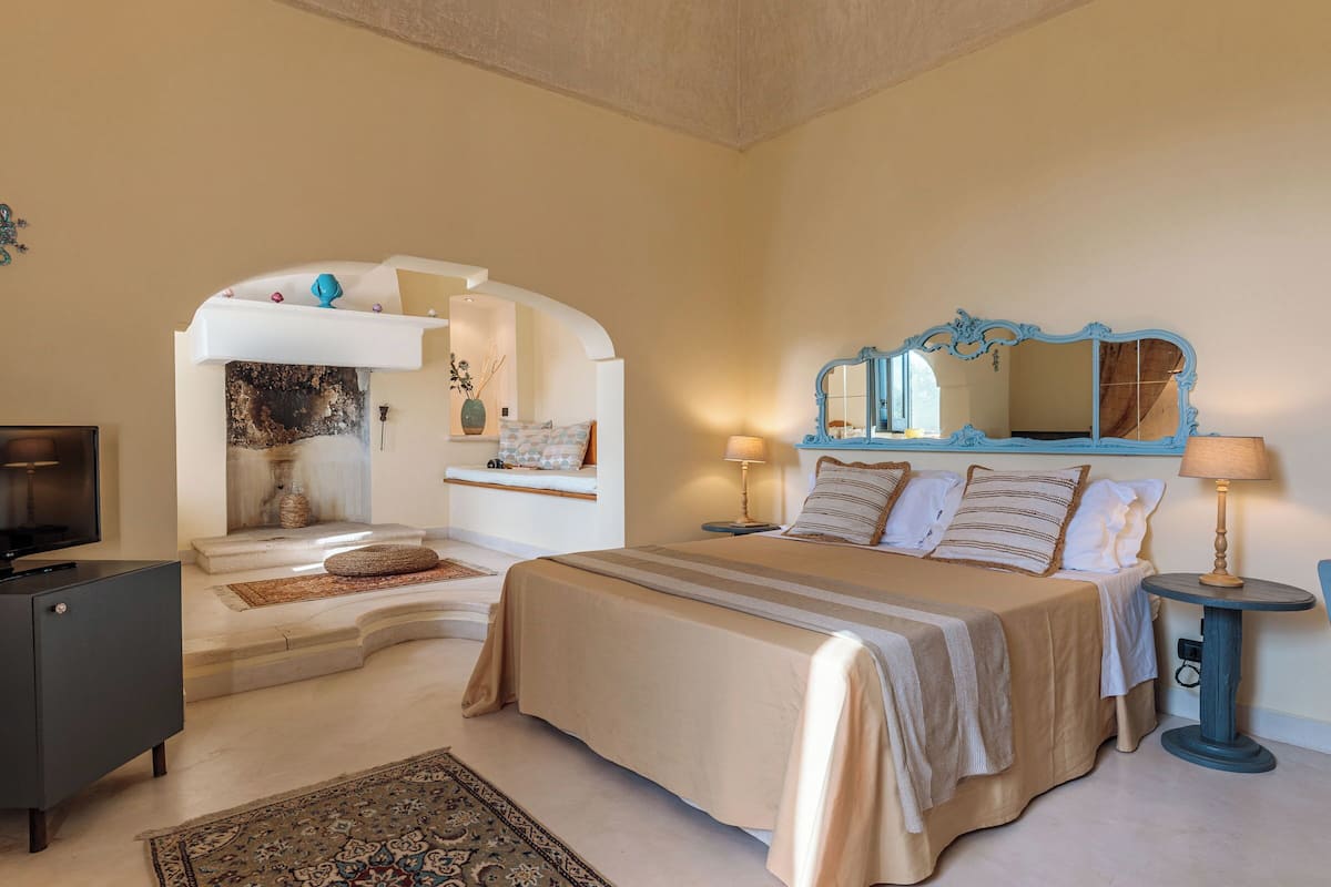 A bedroom with a bed, bedside table, lamp, and a television on a cabinet.