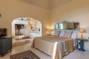 A bedroom with a bed, bedside table, lamp, and a television on a cabinet. - Masseria Brigantino (Fasano)