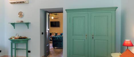 Una habitación con una cama, un armario verde, una mesita con lámpara y un aire acondicionado instalado en la pared.