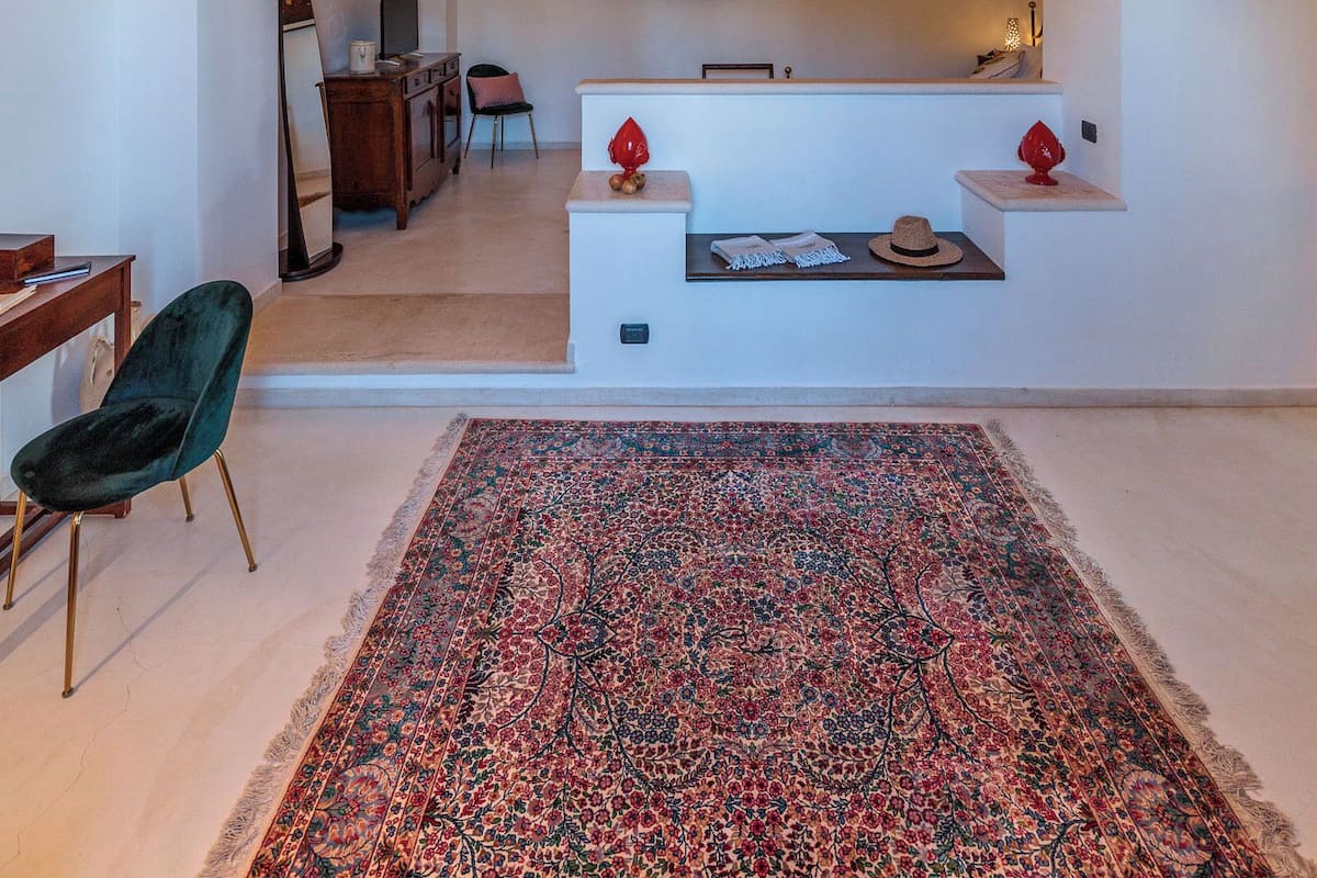 A spacious living area with a high arched stone ceiling, a large patterned rug, and a seating area with a small table and chairs.