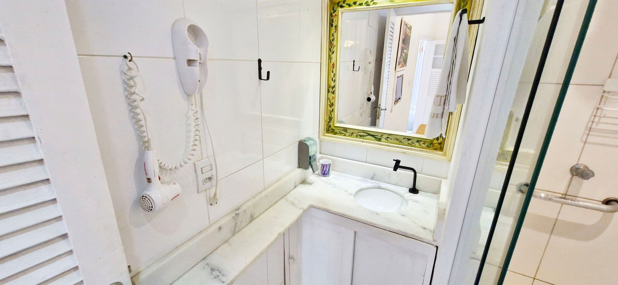 Un bagno con un lavandino bianco, uno specchio con cornice dorata e un asciugacapelli fissato a parete.