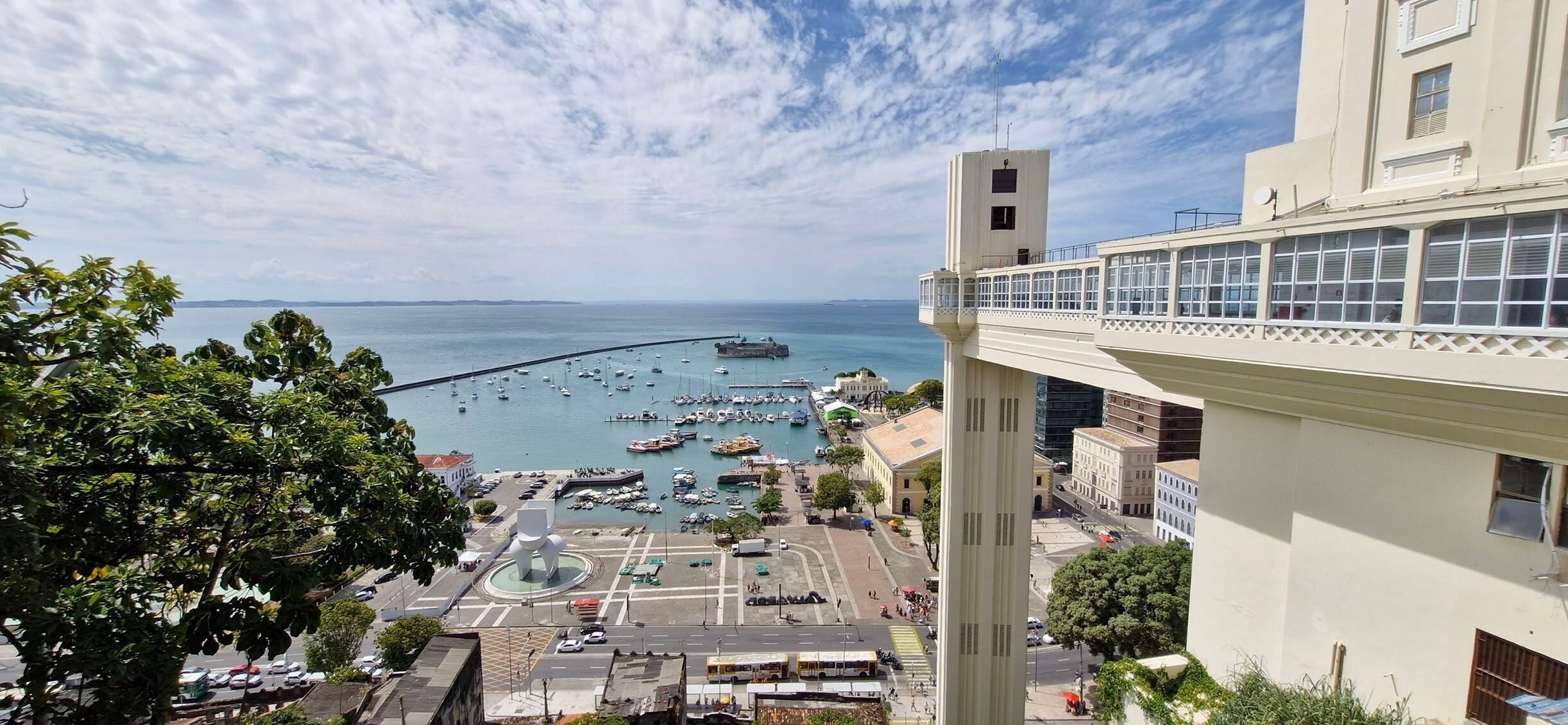 A coastal cityscape with a marina, buildings, and a prominent tower.