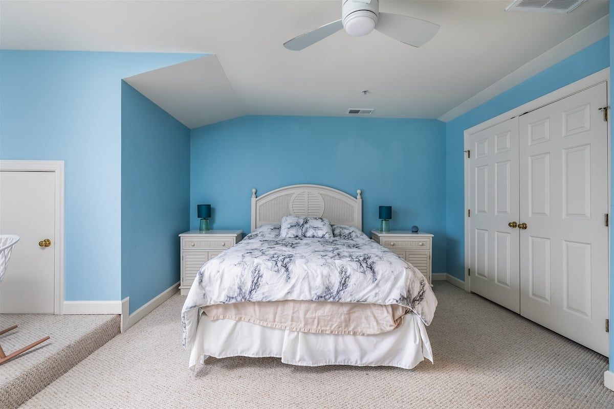 Une chambre à coucher comprenant un lit, des tables de chevet, un ventilateur de plafond et une armoire.