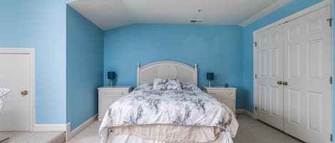 Une chambre à coucher comprenant un lit, des tables de chevet, un ventilateur de plafond et une armoire.