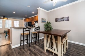A modern kitchen with wooden cabinets, a bar area, and a dining table with bar stools. - Mini Weeks Stays Available Sunset Island 40 Sunset (Ocean City)