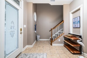 A hallway with a door, a staircase, a wall-mounted light fixture, and a decorative shelf with a bird sculpture. - Mini Weeks Stays Available Sunset Island 40 Sunset (Ocean City)
