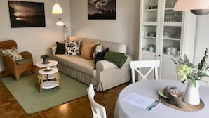 A living room with a sofa, armchairs, a dining table with a vase, and a cabinet with dishes. - Haus Am Apfelweg – Apartment Jonagold, 70 sqm, lake view, private terrace, Wi-Fi (Immenstaad am Bodensee)