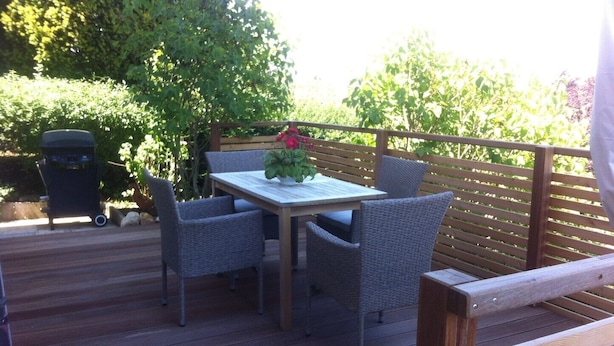 A wooden deck with a table and chairs, surrounded by greenery. - Haus Am Apfelweg – Apartment Jonagold, 70 sqm, lake view, private terrace, Wi-Fi (Immenstaad am Bodensee)