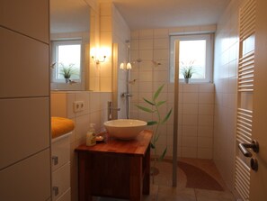 Ett badrum med ett handfat i trä, en stor spegel, en tvättställ, en dusch och en krukväxt.