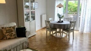 A living room with a sofa, a dining table with chairs, a cabinet with glass doors, and a radiator. - Haus Am Apfelweg – Apartment Jonagold, 70 sqm, lake view, private terrace, Wi-Fi (Immenstaad am Bodensee)