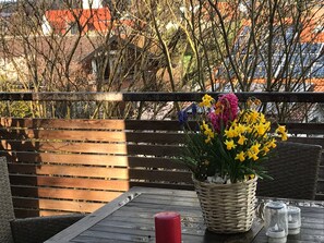 Ett träbord med en korg av rotting som innehåller gula blommor, ett rött ljus samt salt- och pepparkar.