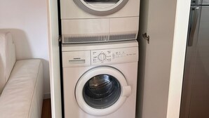 Ein kleiner, weißer Waschraum mit zwei übereinander gestapelten Waschmaschinen und einem modernen, edlen Kühlschrank daneben.
