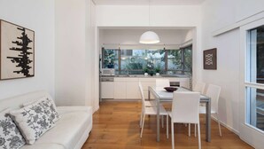 Eine moderne Küche mit weißen Schränken, eine Essecke mit weißem Tisch und Stühlen sowie ein großes Fenster mit Blick auf Grünflächen.