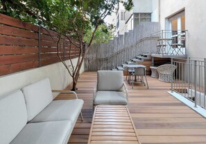 Une terrasse en bois avec un canapé et des fauteuils, un escalier et un balcon également équipé de fauteuils.