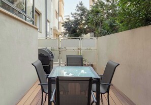 Un tavolo con piano in vetro e quattro sedie in un patio esterno, circondato da un muretto e vegetazione.