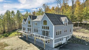 A two-story house with a balcony, surrounded by trees and a gravel driveway. - Huge Luxury Home, Hot Tub, Movie Theater, Mountain Views (Campton)
