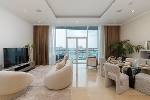 A modern living room with a large flat-screen TV, a beige sofa, and a dining area with a glass table and chairs. - Prime 3BR w/ Beach Access at the Palm (Dubai)