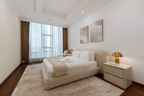 A modern hotel room with a large bed, a nightstand, a lamp, and a view of the city through large windows. - Prime 3BR w/ Beach Access at the Palm (Dubai)
