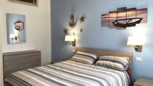 A bedroom with a bed, two bedside tables, a nightstand, a wall-mounted lamp, and a framed picture. - The Sailor's house (Alghero)