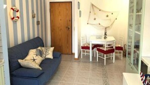 A room with a blue sofa, a wooden door, a white table with chairs, and a cabinet with glass doors. - The Sailor's house (Alghero)