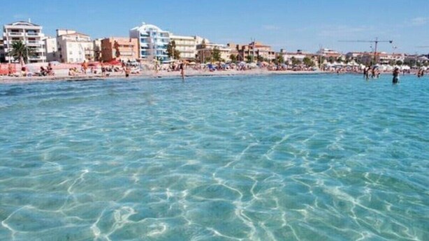 A beach with clear water, buildings, and people. - The Sailor's house (Alghero)