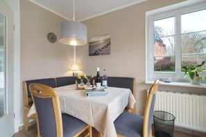Un comedor con una mesa dispuesta para dos personas, un reloj, una lámpara y una ventana con vistas al exterior.
