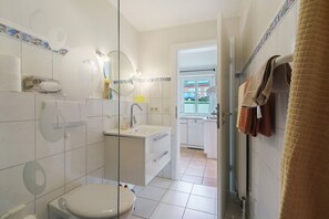 Un baño con inodoro, lavamanos y espejo, junto a una zona de cocina.