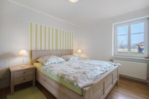 Un dormitorio con cama, mesita de noche, lámpara y ventana.