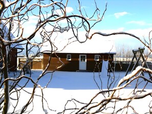 Una cabaña de madera con techo nevado, un garaje y un patio cercado.