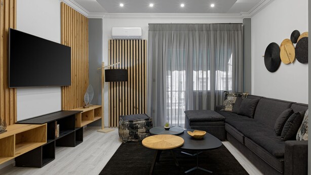 A modern living room with a flat-screen TV, wooden shelving, a grey sofa, and a large window with grey curtains. - Acropolis Deluxe Apartment, Apartment (Athens)
