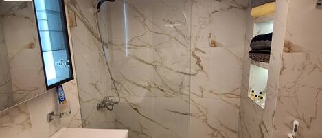 Un baño moderno con piso de mármol, un lavamanos blanco con un espejo encima y una zona de ducha.