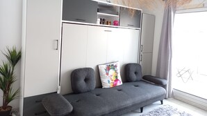 Un salon moderne avec un canapé gris, un meuble blanc et une grande fenêtre donnant sur un beau paysage.