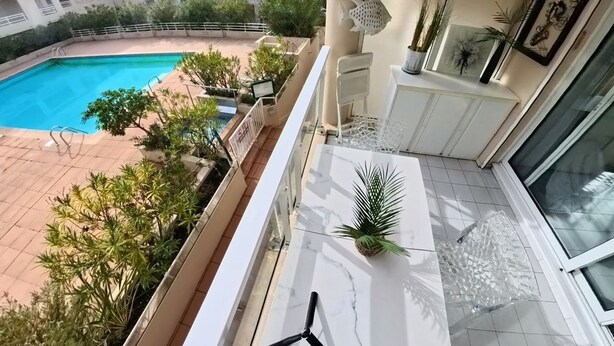 Un balcon donnant sur une piscine, agrémenté de plantes en pot et doté d’un sol carrelé.
