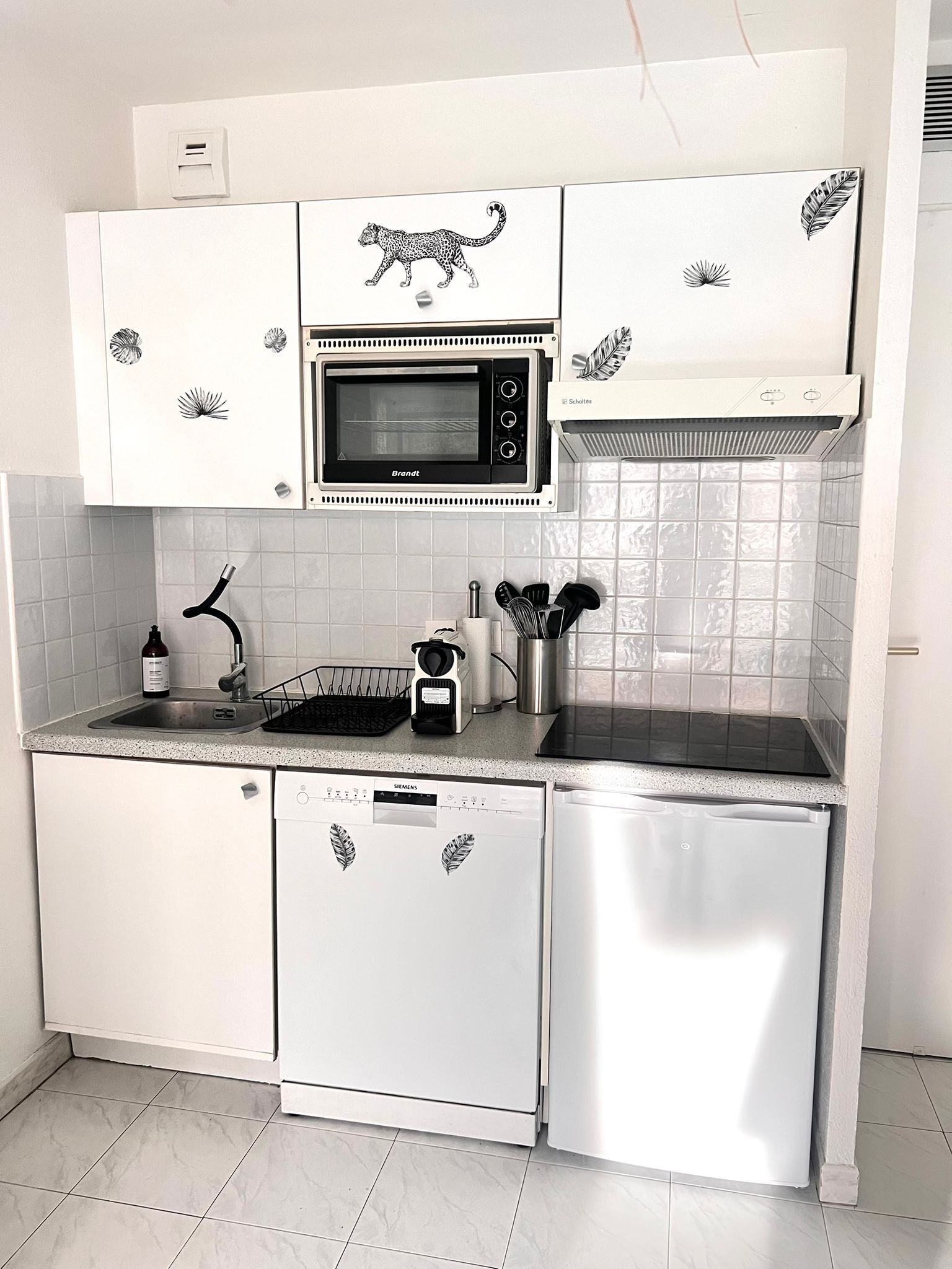 A compact kitchen with white cabinetry, a built-in microwave, a dishwasher, and a sink.