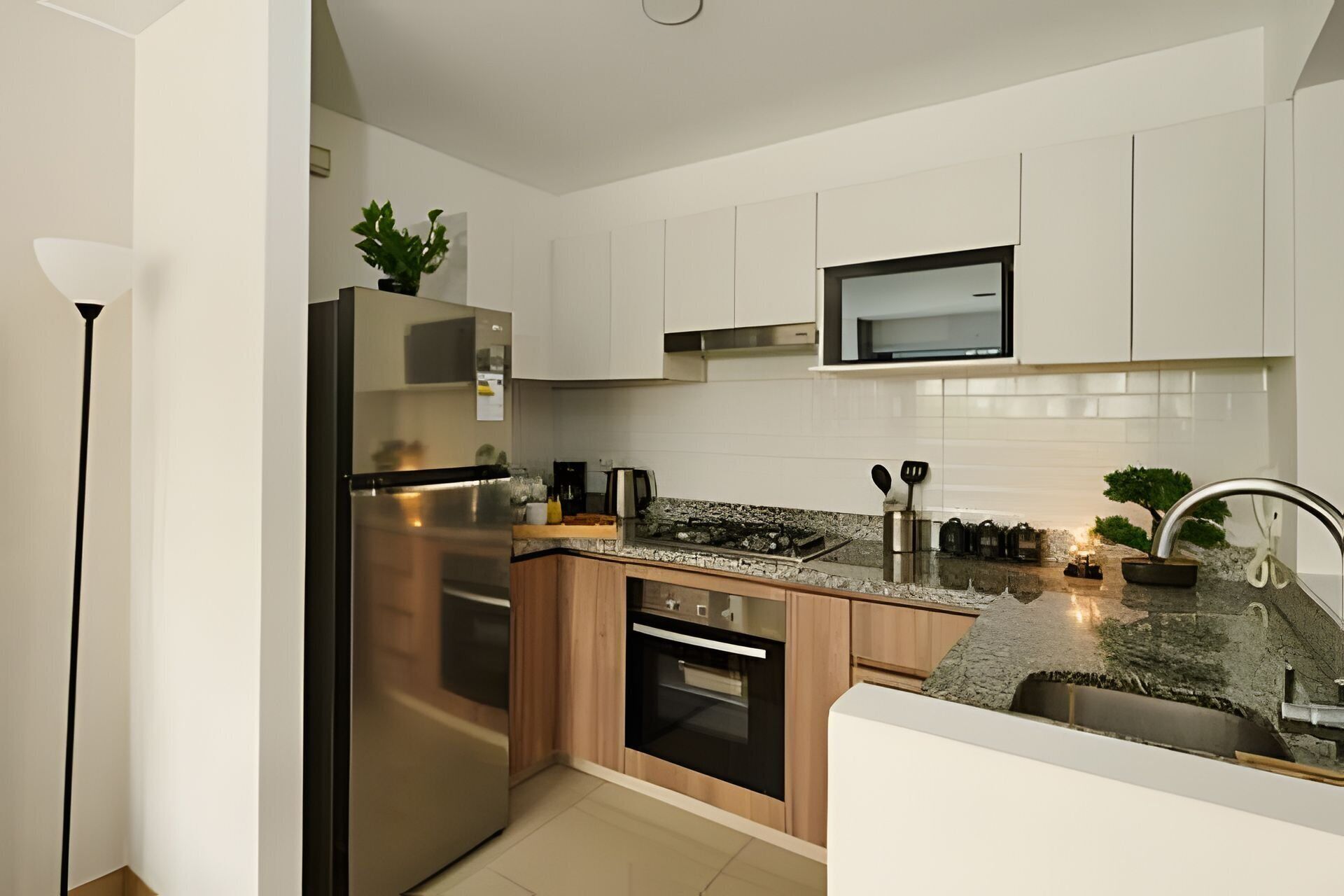 A modern kitchen with white cabinets, stainless steel appliances, a granite countertop, and a small potted plant.