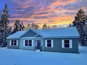 Ein zweistöckiges Haus mit einem Satteldach, umgeben von schneebedeckten Bäumen.