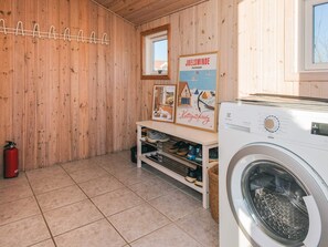 Ein Waschraum mit einer Waschmaschine, einem Schuhregal, einem Feuerlöscher und einem Poster an der Wand.